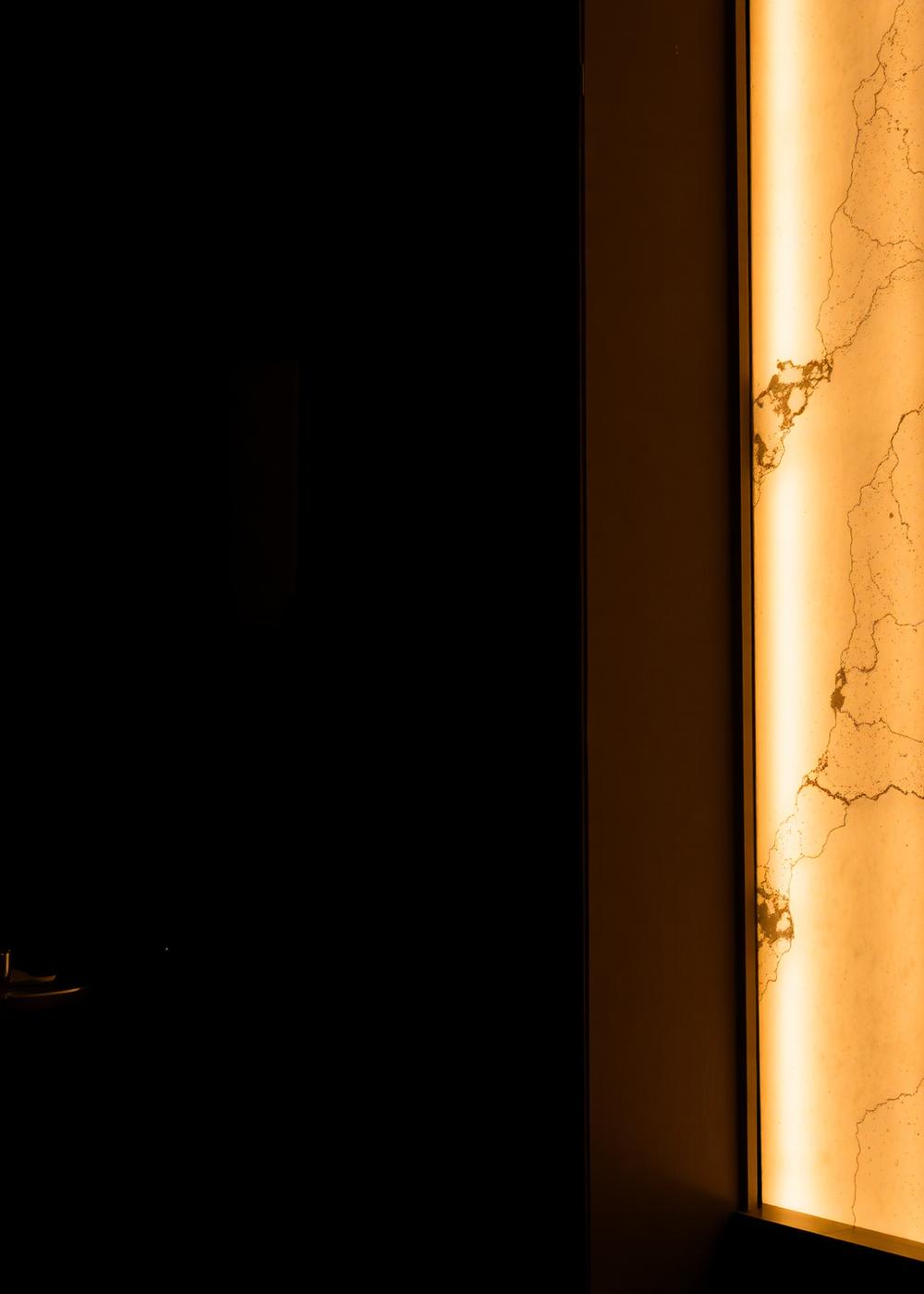 Backlit alabaster wall panel casting warm light across a dark restaurant interior